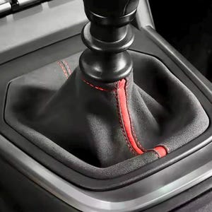 Puede incluir: Primer plano de una funda de palanca de cambios de coche de cuero negro con costuras rojas.