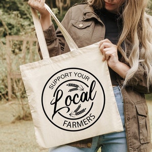 May include: A white canvas tote bag with black text that reads "Support Your Local Farmers" in a circle with wheat stalks.