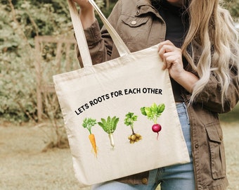 May include: A white canvas tote bag with the text "Lets Roots for Each Other" printed in black. The bag features a graphic of four different vegetables: a carrot, a turnip, a potato, and a beet.
