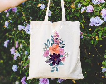 May include: A white canvas tote bag with a floral design featuring pink, purple, and orange flowers. The bag has a long handle and is perfect for carrying everyday essentials.
