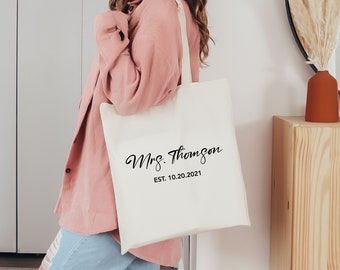 May include: White canvas tote bag with black text that reads "Mrs. Thomson Est. 10.20.2021".