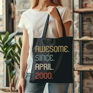 May include: Black tote bag with the text "Awesome. Since. April. 2000." in a retro font with colorful stripes.