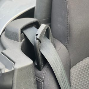 Può includere: Primo piano di una fibbia e di una cintura di sicurezza grigie in un'auto. La cintura di sicurezza è allacciata, con la cinghia che si estende attraverso il telaio. L'interno circostante è in tessuto e plastica grigi.