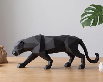 May include: A black geometric panther sculpture with a faceted, low-poly design. The panther is depicted in a walking stance with its head lowered. The figure features sharp, angular planes and a matte finish, showcasing a stylized, modern form.
