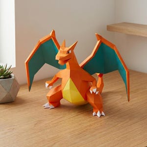May include: A low-poly papercraft figure of the orange dragon-like creature Charizard with teal-colored wings, a yellow belly, and white claws. The figure features sharp geometric angles and a standing pose with wings spread wide.