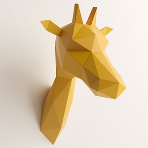 Op de afbeelding: Een gele wandsculptuur van een giraffekop, opgebouwd met een geometrisch low-poly ontwerp. Het stuk heeft scherpe, hoekige facetten die de snuit, oren en ossiconen vormen, wat zorgt voor een gestructureerde, driedimensionale weergave.