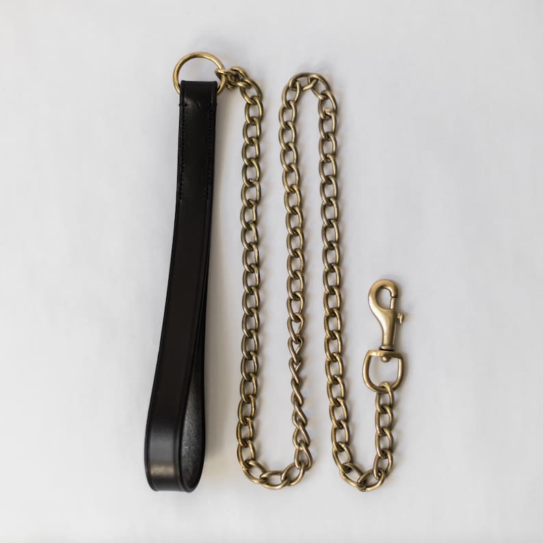 May include: A black leather lead with a gold chain and a gold clasp.