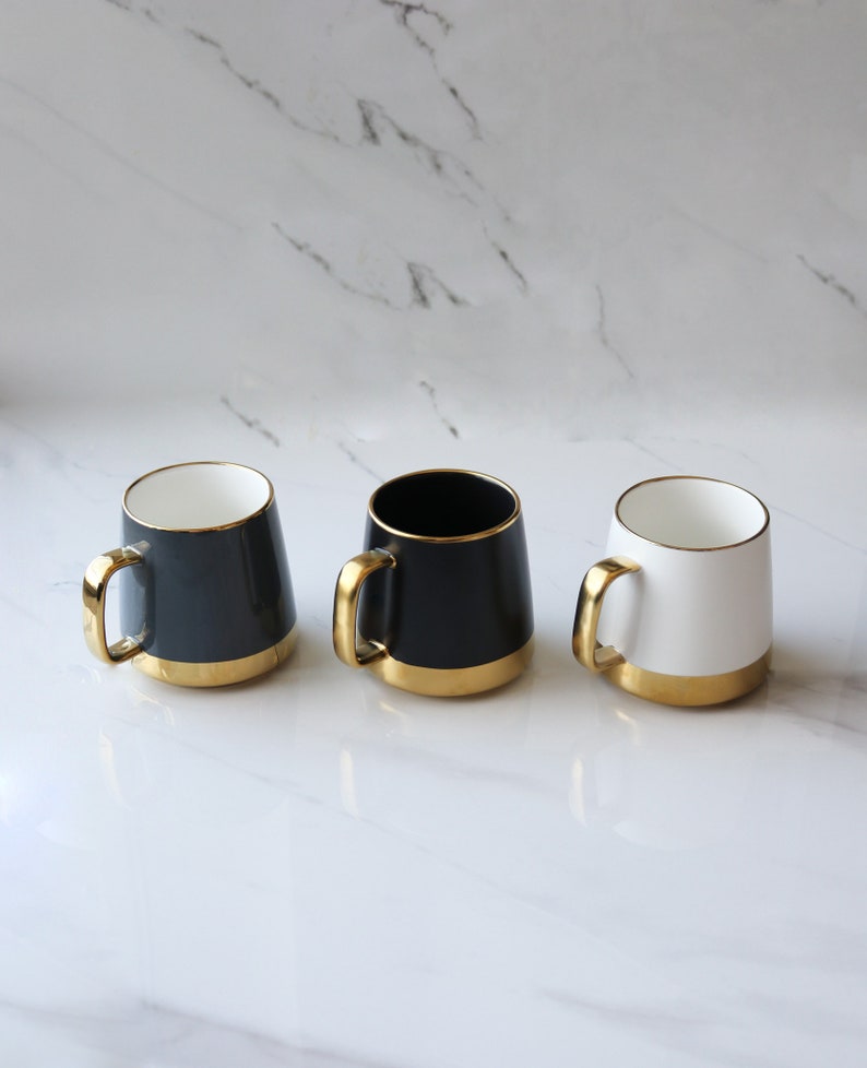 May include: Three ceramic mugs with gold rims. The mugs are black, white, and gray.