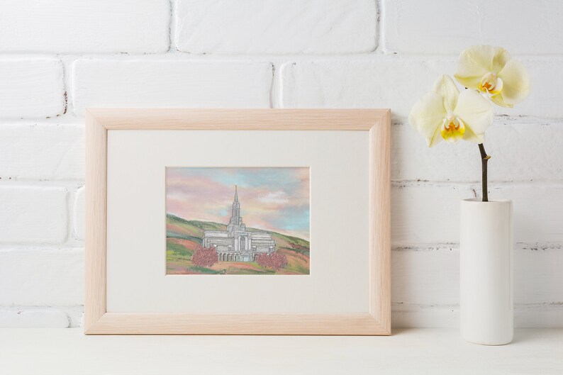 Peut inclure: Une impression encadr&eacute;e d'une peinture &agrave; l'aquarelle repr&eacute;sentant un b&acirc;timent d'&eacute;glise blanc avec un haut clocher, entour&eacute; d'arbres et de collines. Le ciel est rose et bleu p&acirc;le.
