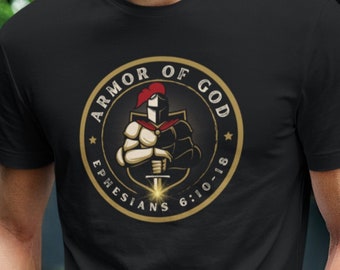 May include: Black t-shirt featuring a gold and black circular design with the text "ARMOR OF GOD" and "EPHESIANS 6:10-18". The design depicts a knight in armor. The person is wearing blue jeans and a watch.