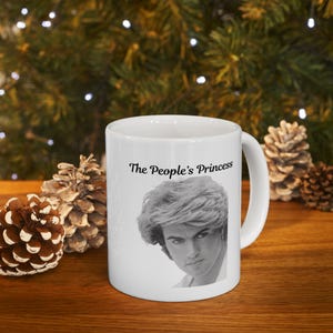May include: White ceramic mug with a black and white photo of a person with the text "The People's Princess" printed on the front.