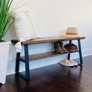 May include: A wooden bench with black metal legs and a shelf. The bench has a white throw pillow and a straw hat on top. There are shoes on the shelf.