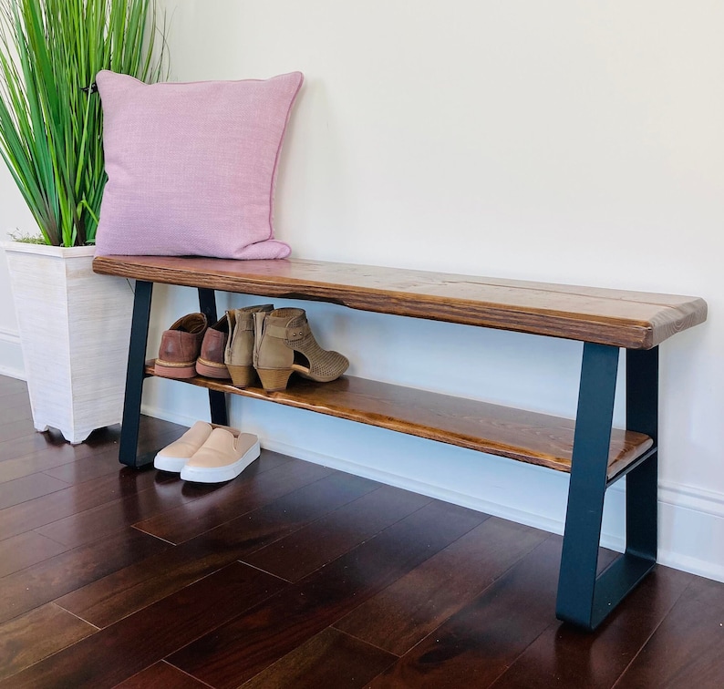 May include: A wooden bench with a black metal frame and a shelf underneath. The bench has a natural wood finish and is made of reclaimed wood. The bench is sitting on a hardwood floor.
