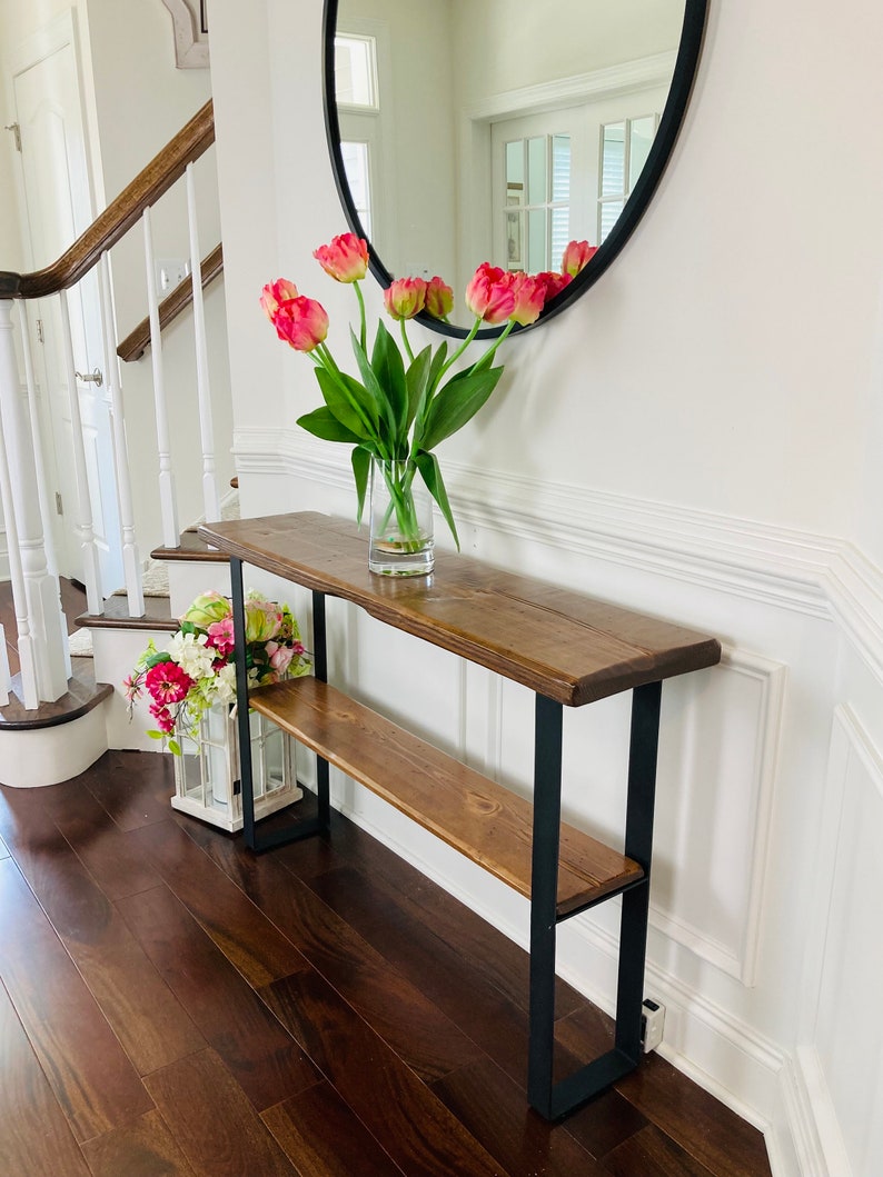 May include: A wooden console table with a black metal frame and two shelves. The table is decorated with a vase of pink tulips and a small arrangement of pink flowers.
