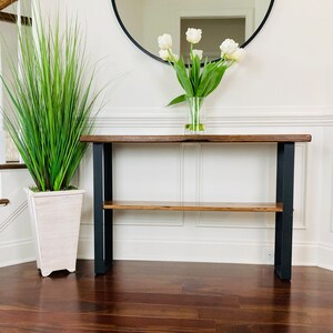 May include: A wooden console table with a black metal frame and a shelf. The table has a natural wood finish and is decorated with a vase of white tulips.