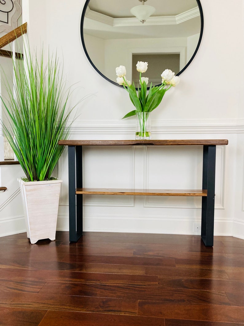 May include: A wooden console table with a black metal frame and a shelf. The table has a natural wood finish and is decorated with a vase of white tulips.