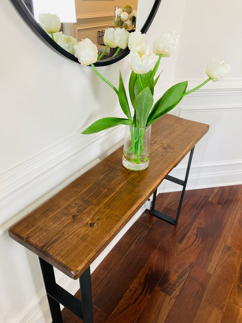 May include: A wooden console table with black metal legs. The table has a dark brown stain and is topped with a vase of white tulips.