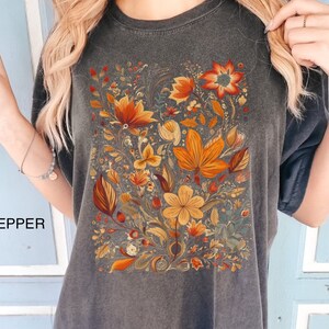 May include: A dark gray oversized t-shirt with a floral print in shades of orange, yellow, and red. The print features a variety of flowers and leaves.