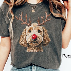 K&ouml;nnte beinhalten: Eine Frau tr&auml;gt ein graues T-Shirt mit einem braunen Hund, der eine rote Nase und Geweih tr&auml;gt. Der Text "Pepper" ist auf dem T-Shirt sichtbar. Die Frau tr&auml;gt eine blaue Jeans und wei&szlig;e Turnschuhe. Der Text "Lovin What U Wear" ist in der rechten unteren Ecke des Bildes sichtbar.
