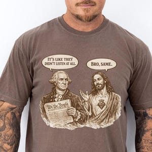 Może przedstawiać: Koszulka w kolorze espresso z grafiką George'a Washingtona i Jezusa w dymkach. Washington trzyma dokument z napisem "We the People". Dymki m&oacute;wią "It's like they didn't listen at all" i "Bro, same."