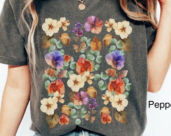May include: A charcoal gray t-shirt with a floral print featuring a variety of colors, including purple, orange, yellow, and green. The text "Pepper" is visible on the right side of the image.