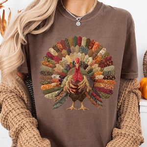 May include: Espresso-colored t-shirt featuring a detailed turkey design with a patchwork-style tail in autumn colors. The shirt has short sleeves and is paired with a brown cardigan. The text "Espresso" is visible.