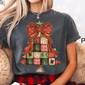 May include: A dark gray t-shirt featuring a Christmas tree design. The tree is composed of patchwork squares in red, green, and white, topped with a red bow and a gold star. The shirt has the word "Pepper" printed on the side.
