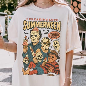 May include: Ivory t-shirt featuring the phrase "I FREAKING LOVE SUMMERWEEN" and a graphic of horror movie characters with ice cream. The shirt also has the text "CAN I GET SOME ICE SCREAM, PLEASE?"
