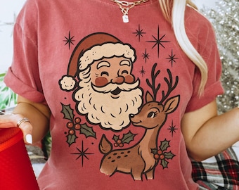 May include: Crimson-colored t-shirt featuring a vintage-style illustration of Santa Claus and a reindeer, surrounded by stars and holly. The text "Crimson" is printed on the shirt, along with the brand name "Lovin What U Wear".