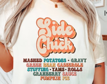 May include: A white t-shirt with a retro-style graphic that says "Side Chick" and lists Thanksgiving side dishes: mashed potatoes, gravy, green bean casserole, stuffing, yams, rolls, cranberry sauce, and pumpkin pie.