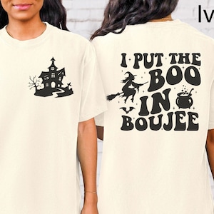 May include: Ivory short-sleeved t-shirt with a black graphic of a haunted house on the front and the text "I put the boo in boujee" on the back.