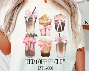 May include: A white t-shirt with a graphic of six iced coffee drinks with pink bows. The text "ICED COFFEE CLUB EST. 2006" is printed below the graphic.
