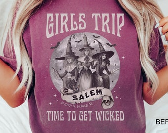 May include: A purple t-shirt with a graphic of three witches in front of a full moon with bats flying around it. The text "Girls Trip Salem Time to Get Wicked" is printed on the shirt.