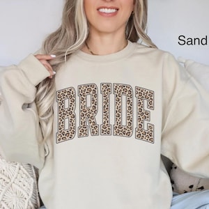May include: A sand-colored sweatshirt with the word "BRIDE" printed in a leopard print pattern.