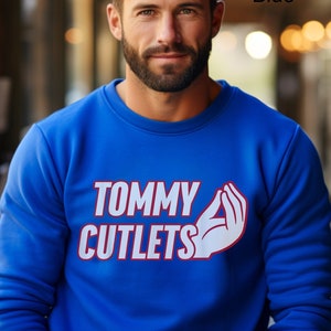 May include: A royal blue sweatshirt with the text "TOMMY CUTLETS" in white with a red outline and a white hand gesture.