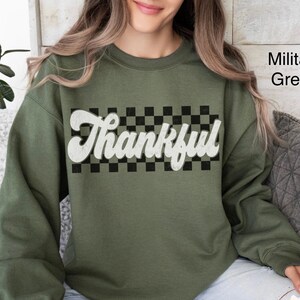 May include: A green sweatshirt with a black and white checkered pattern and the word "Thankful" in white lettering.