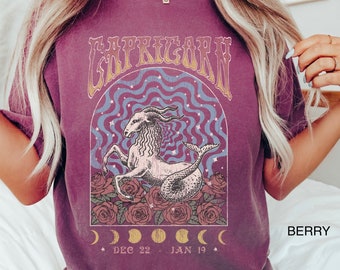 Könnte beinhalten: Ein lila T-Shirt mit einem Vintage-Grafikdruck eines Steinbock-Sternzeichen. Die Grafik zeigt ein Seeziegen-Wesen mit einem Schwanz, umgeben von Rosen und einem Halbmond-Design. Der Text "Capricorn" ist in einer fetten, Retro-Schriftart über der Grafik gedruckt. Die Daten "Dec 22 - Jan 19" sind unter der Grafik gedruckt.