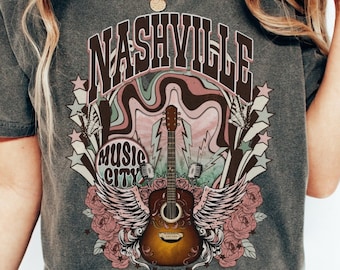 May include: A gray t-shirt with a vintage-style graphic of a guitar with wings and the text "Nashville Music City".