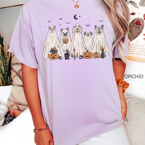 Peut inclure: Un t-shirt violet avec un motif de cinq chiens habill&eacute;s en fant&ocirc;mes pour Halloween. Les chiens tiennent des citrouilles et des sacs de bonbons. Le motif comprend &eacute;galement une lune croissante, des &eacute;toiles et un cimeti&egrave;re.