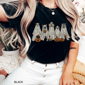 Peut inclure: T-shirt noir avec un motif de cinq chiens habill&eacute;s en fant&ocirc;mes tenant des citrouilles et des bougies. Le texte "BLACK" est visible dans le coin inf&eacute;rieur gauche de l'image.