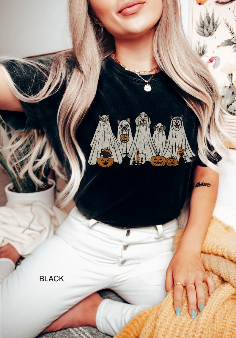 Peut inclure: T-shirt noir avec un motif de cinq chiens habill&eacute;s en fant&ocirc;mes tenant des citrouilles et des bougies. Le texte "BLACK" est visible dans le coin inf&eacute;rieur gauche de l'image.