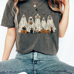 Peut inclure: Un t-shirt gris avec un motif vintage de chiens d&eacute;guis&eacute;s en fant&ocirc;mes pour Halloween. Les chiens tiennent des citrouilles et des sacs de bonbons. Le motif comprend &eacute;galement un chat noir portant un chapeau de sorci&egrave;re.