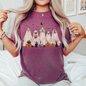 Peut inclure: T-shirt violet avec un motif de chiens habill&eacute;s en fant&ocirc;mes pour Halloween. Les chiens tiennent des citrouilles et il y a des chauves-souris et un croissant de lune en arri&egrave;re-plan.