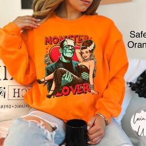 Peut inclure: Sweat-shirt orange avec un imprim&eacute; graphique d'un couple de monstres. Le texte sur le t-shirt dit "Monster Lover".