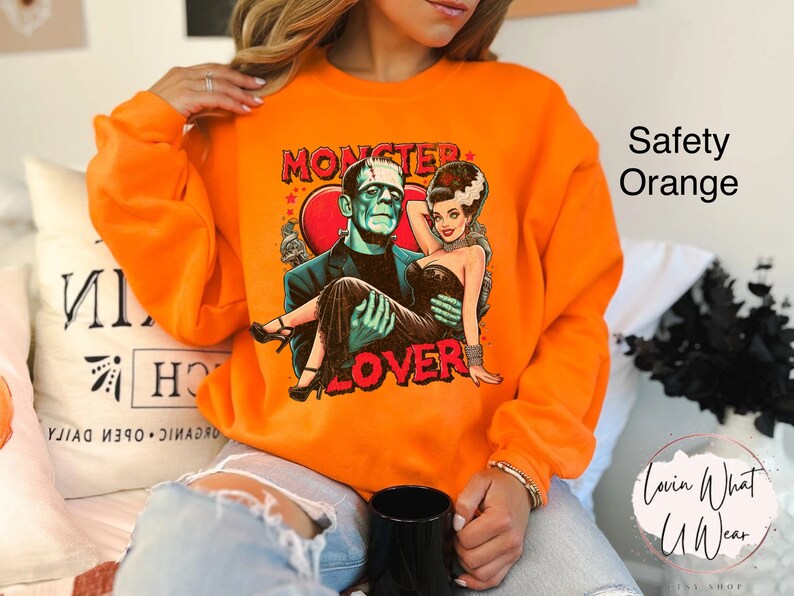 Peut inclure: Sweat-shirt orange avec un imprim&eacute; graphique d'un couple de monstres. Le texte sur le t-shirt dit "Monster Lover".