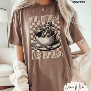 May include: A brown t-shirt with a skeleton in a coffee cup graphic and the text "More Espresso Less Depresso".