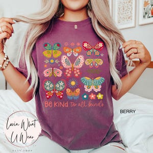 May include: Purple t-shirt with a colorful butterfly design and the text "Be Kind to all kinds".