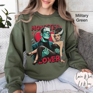 Peut inclure: Un sweat-shirt vert avec un imprim&eacute; graphique d'un couple de monstres. Le texte sur le sweat-shirt dit "Monster Lover".