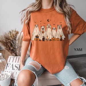 May include: Orange t-shirt featuring a graphic of five dogs dressed as ghosts for Halloween. The dogs are holding pumpkins and a cat is sitting in front of them. The graphic is in a vintage style.