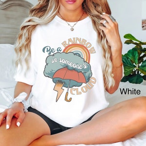 May include: White t-shirt with a graphic of a rainbow in a cloud with the text "Be a rainbow in someone's cloud".